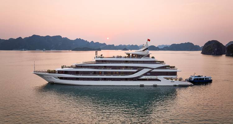 Elegante crucero de lujo al atardecer entre las islas de piedra caliza de la Bahía de Ha Long.