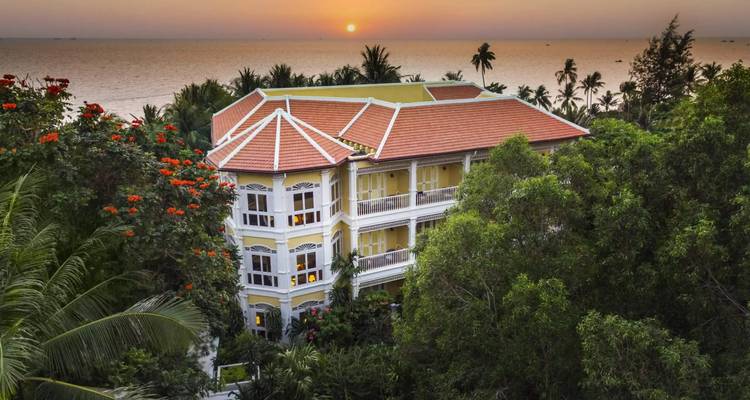 Hotel boutique de estilo colonial rodeado de vegetación tropical con vistas al mar al atardecer.