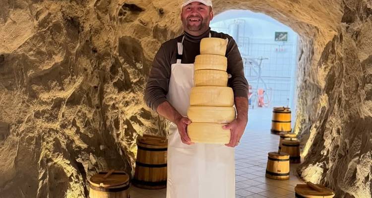 Homme dans une fromagerie tenant des meules de fromage empilées.