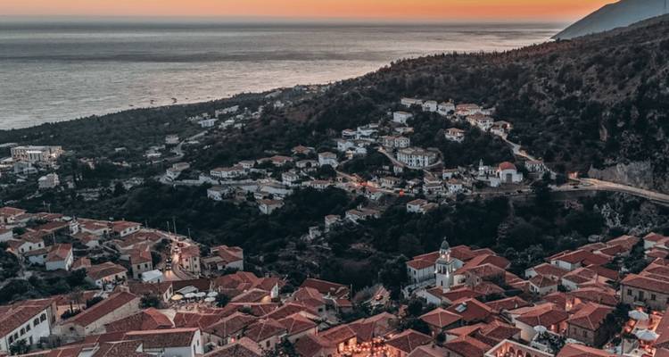 Vue aérienne d'un village côtier avec des toits de tuiles au coucher du soleil.