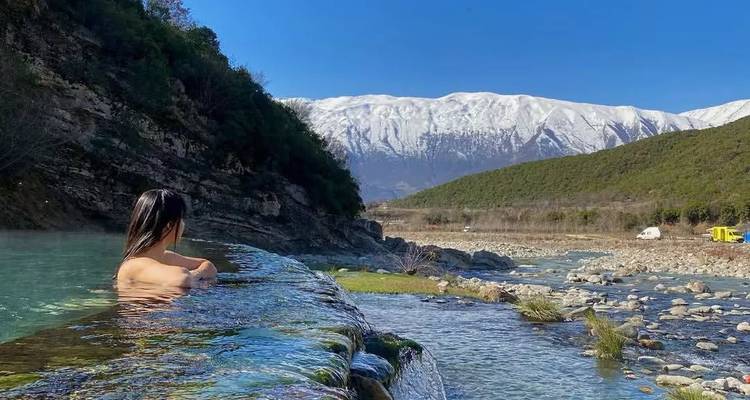 Femme dans une source chaude naturelle avec des montagnes en arrière-plan.