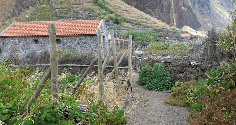 Maison en pierre rustique dans un paysage rural avec un sentier de terre.