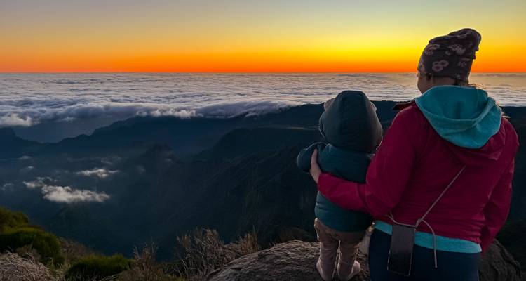 Person with a child watching the sunset over the clouds from a mountain.