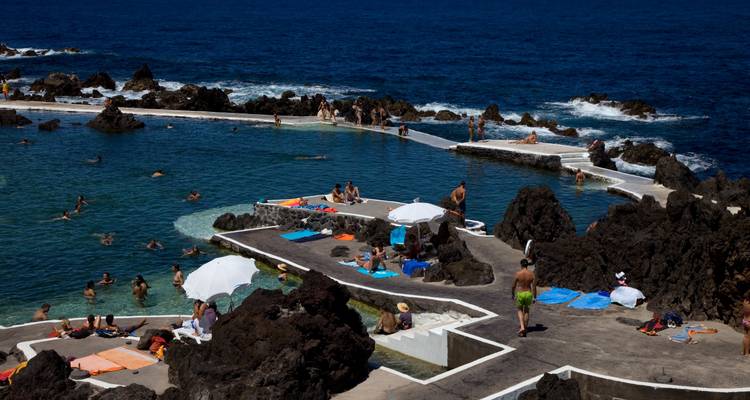 People enjoying natural pools with rocky ocean backdrop.