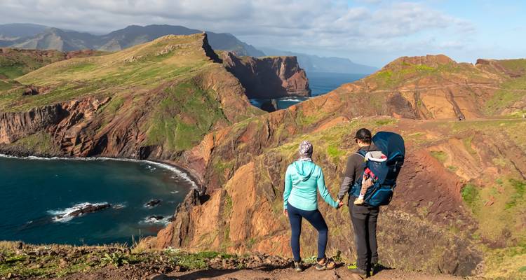 Couple hiking on a scenic coastal path with mountains and sea.