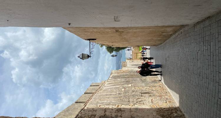 Ruelle étroite en pierre avec des gens qui marchent sous des lanternes suspendues.