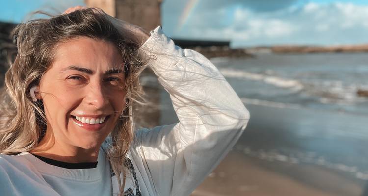 Femme souriante à la caméra avec la plage et un arc-en-ciel en arrière-plan.
