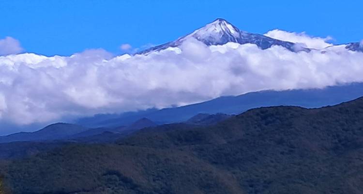 Sommet de montagne couvert de nuages avec des collines boisées.