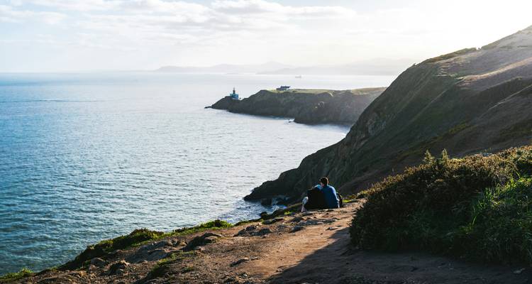 Falaises au bord de mer avec un phare au loin.