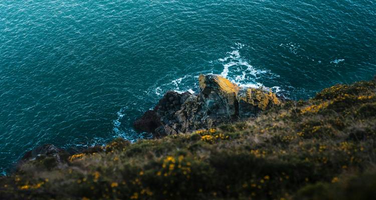 Une falaise rocheuse surplombant l'océan avec des vagues qui se brisent.