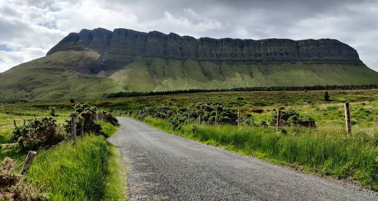 Une route de campagne menant à une montagne sous un ciel nuageux.