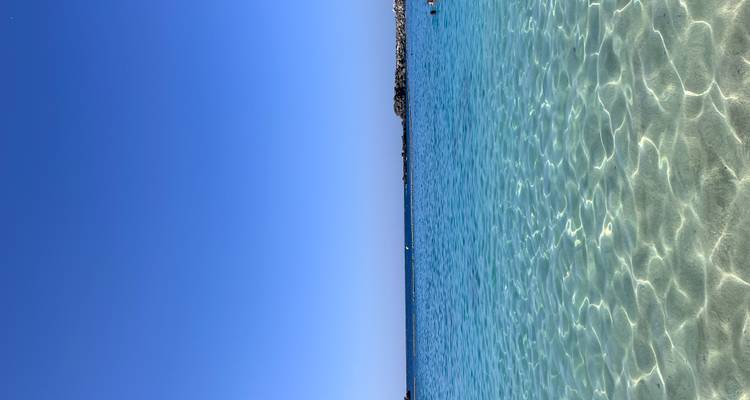 Océan et ciel d'un bleu limpide avec de douces vagues qui viennent lécher le rivage.