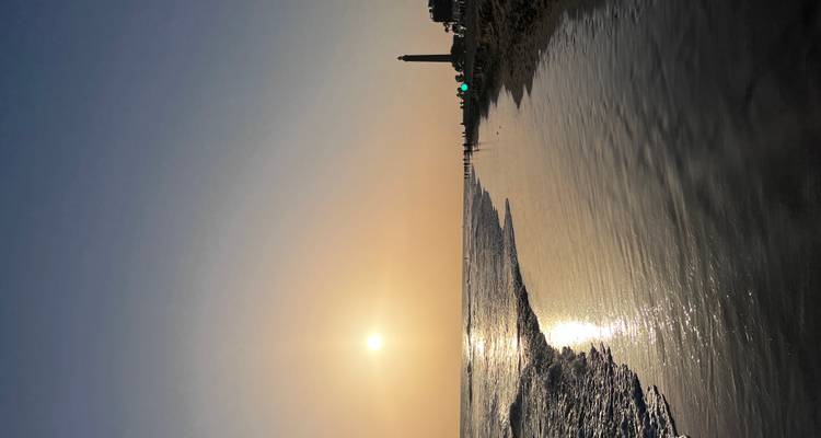 Une scène de plage au coucher du soleil avec des personnes en silhouette et un phare.