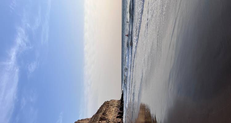 Une plage tranquille avec des vagues et des formations de falaises rocheuses au loin.