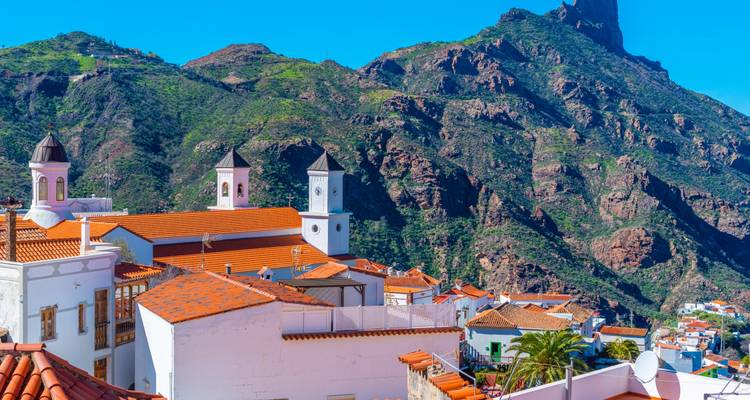 A scenic village with white buildings against a mountain backdrop.