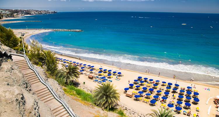 A beach with sun umbrellas and people, clear sea and sandy shore.
