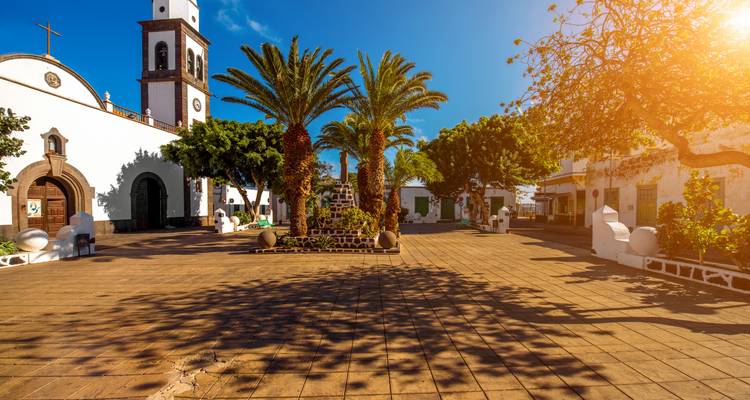 Place avec église et palmiers sous la chaude lumière du soleil.