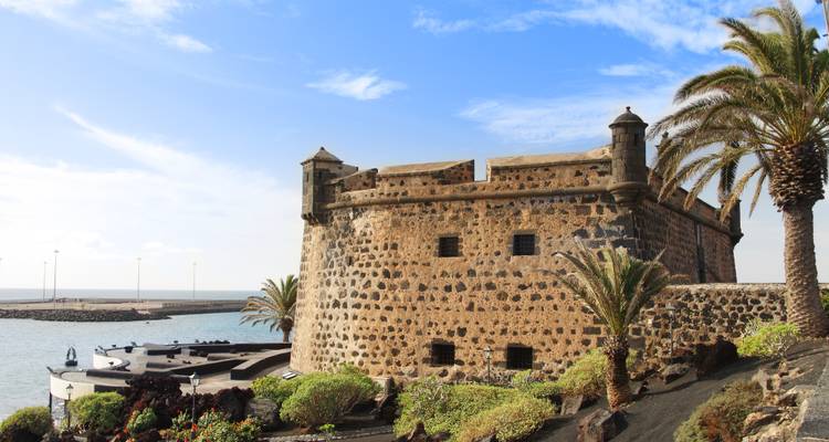 Forteresse historique au bord de la mer avec des palmiers.