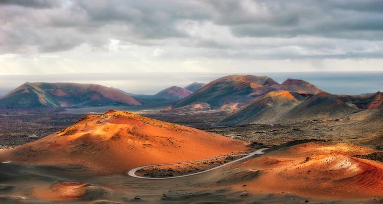 Paysage volcanique avec des montagnes et une route sinueuse sous un ciel nuageux.