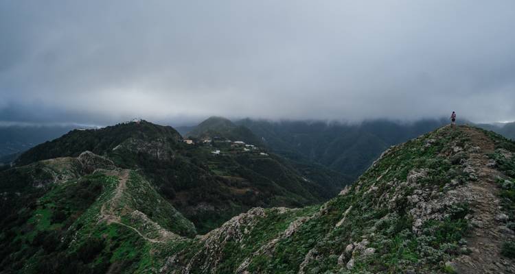 Paysage montagneux avec des nuages menaçants et un terrain verdoyant.