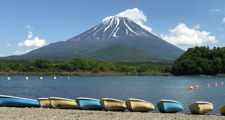 Mount Fuji over a bodies of water with canoes on the shore.