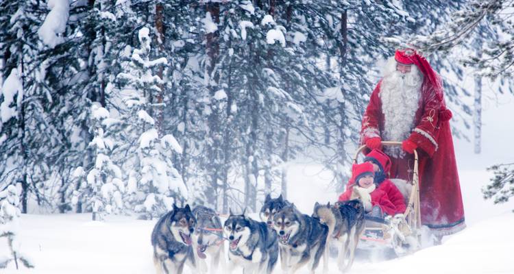 Santa Claus with a child on a sled pulled by huskies in a snowy forest.