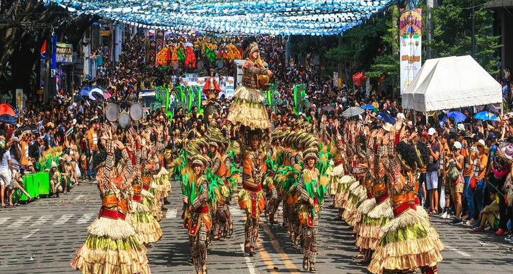 Défilé de rue vibrant avec des danseurs en costumes ornés de plumes se produisant sous un dais de banderoles bleues tandis que les foules bordent l'avenue.