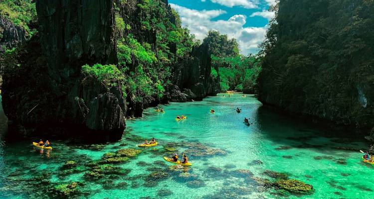 Lagon turquoise cristallin parsemé de kayaks jaunes entouré de falaises calcaires imposantes et de jardins de corail.