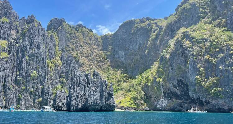D'abruptes falaises calcaires encadrent une mer d'un bleu profond sous un ciel tropical lumineux.