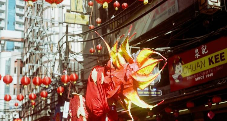 Danse du dragon rouge vif au milieu de lanternes suspendues et des fils électriques animés de la rue de Chinatown.