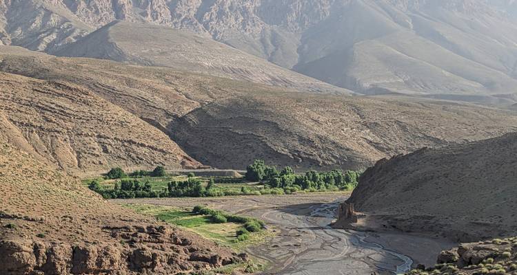 Tal mit einem Fluss, grünen Flecken und trockener Bergkulisse.