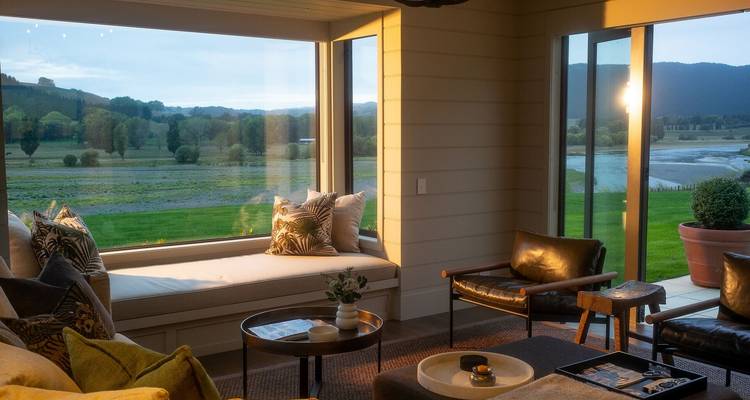 Intérieur douillet d'un lodge de luxe avec des fenêtres panoramiques donnant sur le paysage rural de la Nouvelle-Zélande au crépuscule