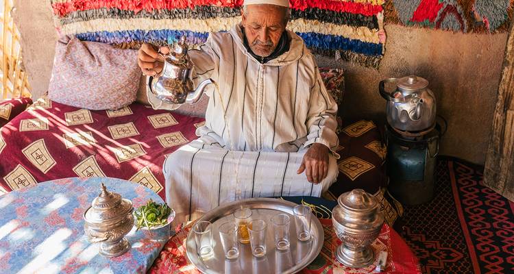 Man in traditional attire pouring tea in a quaint setting.