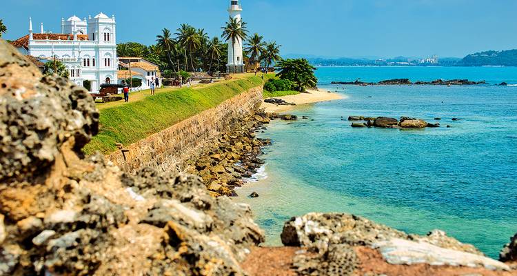 Scenic coastal view, including a lighthouse, palm trees, and striking turquoise water.