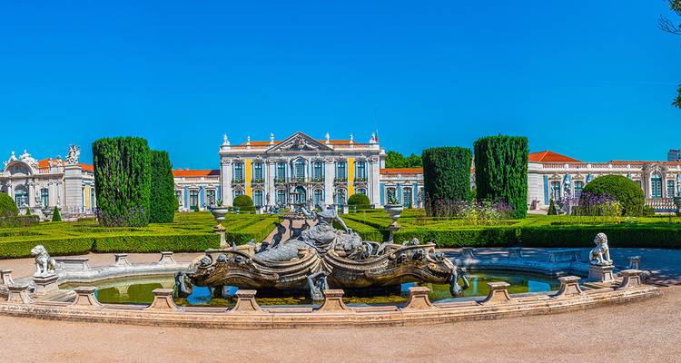 A grand palace with beautiful gardens and a prominent fountain in the foreground.