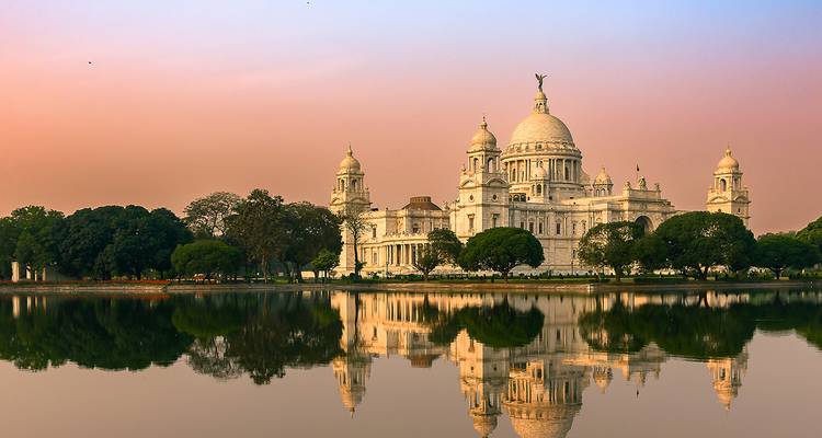 Grand bâtiment colonial avec reflets dans l'eau au coucher du soleil.