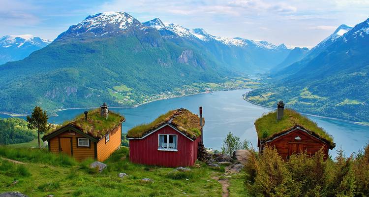View of a fjord with cabins and snow-capped mountains.