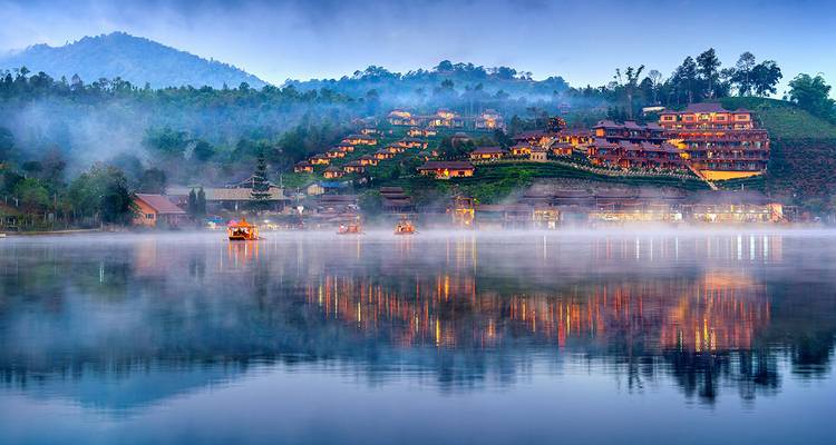 A serene lakeside village with traditional houses on a misty morning.