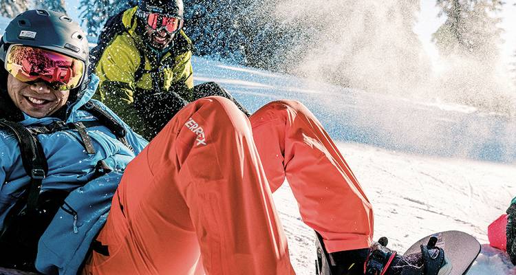 Snowboarders die lachen op een poederige helling terwijl verse sneeuw om hen heen opstuift.