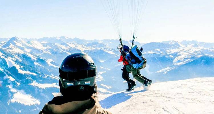 Paragliders die vanaf een sneeuwrijke alpiene bergrug opstijgen met uitgestrekte Oostenrijkse bergketens op de achtergrond