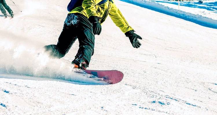 Photo d'action d'un snowboardeur effectuant des virages dans la neige fraîche sur une pente hivernale ensoleillée.