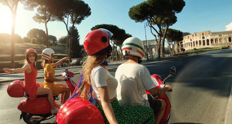 Group of people riding scooters near an ancient amphitheater.