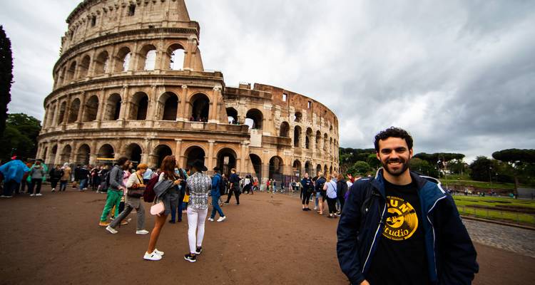 Person smiling near a large amphitheater with tourists.