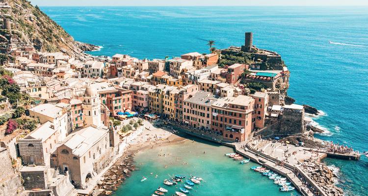 Lumineux village à flanc de falaise de Vernazza surplombant la mer Ligure turquoise avec des bateaux dans le port.