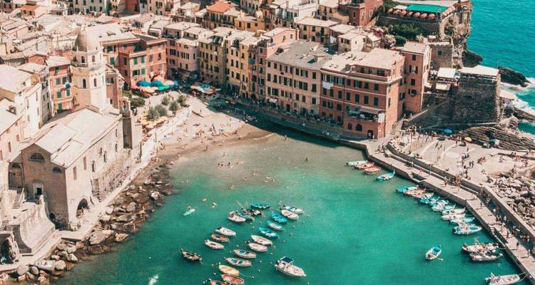 Buntes Küstendorf und kleiner Hafen umgeben von türkisblauem Wasser und vertäuten Booten in Cinque Terre.