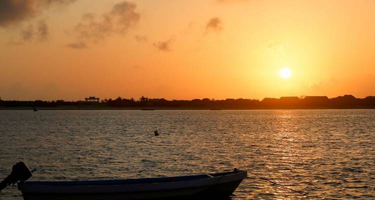 Bateau flottant sur un lac avec un coucher de soleil en arrière-plan.