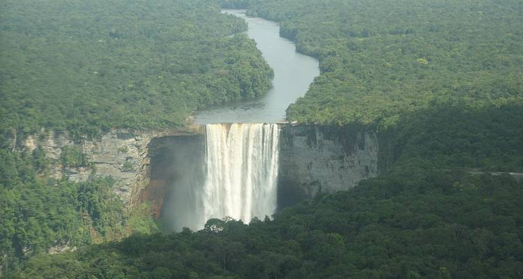 A spectacular waterfall flowing from a forested cliff into a river.