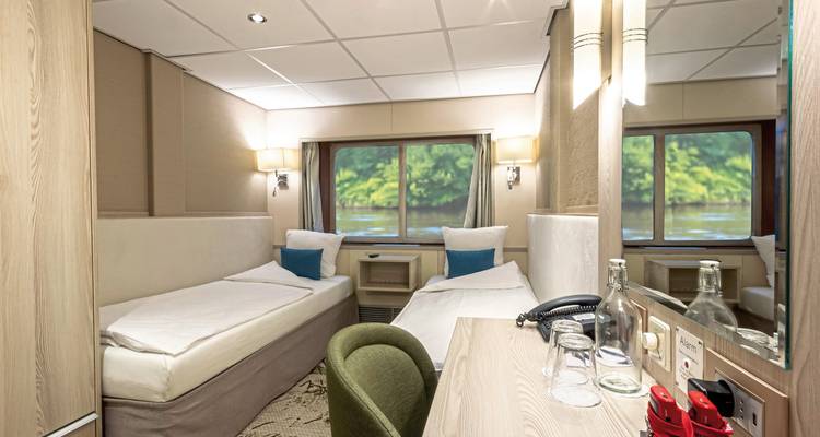 Interior of a small cruise cabin with twin beds and river view.