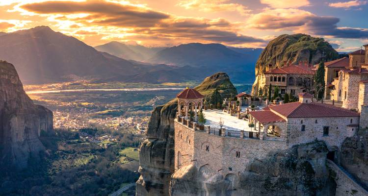 Monastery on a cliff with a scenic mountain view at sunset.
