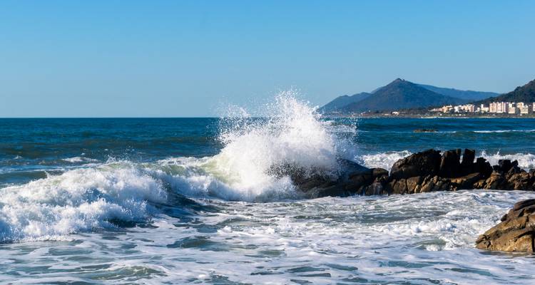 Des vagues océaniques qui se brisent contre les rochers avec des montagnes en arrière-plan.
